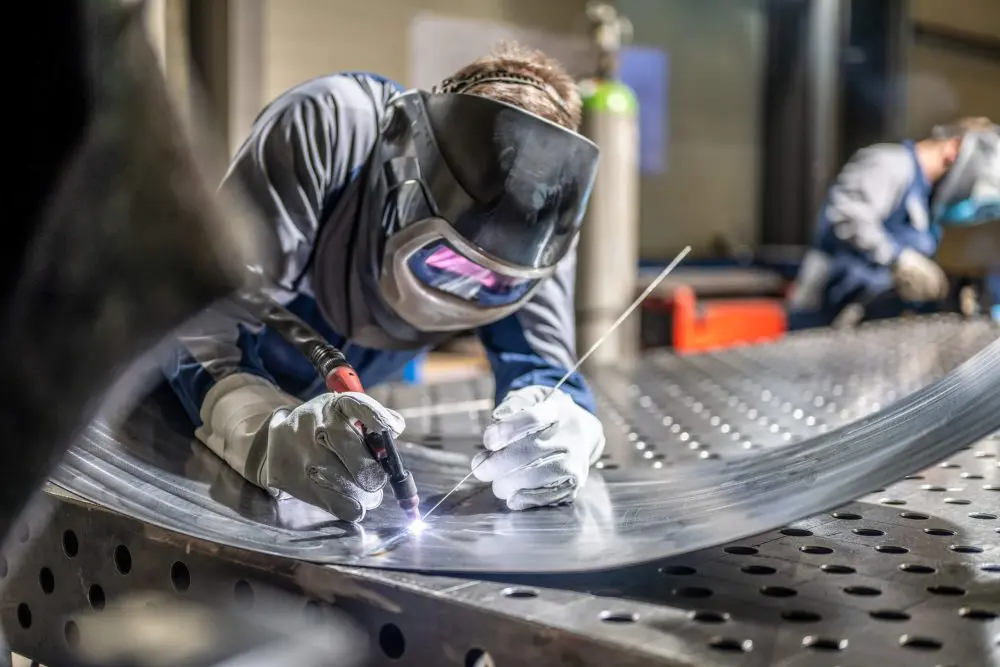 Un soudeur de sexe masculin portant un casque travaillant avec un chalumeau à souder en usine.